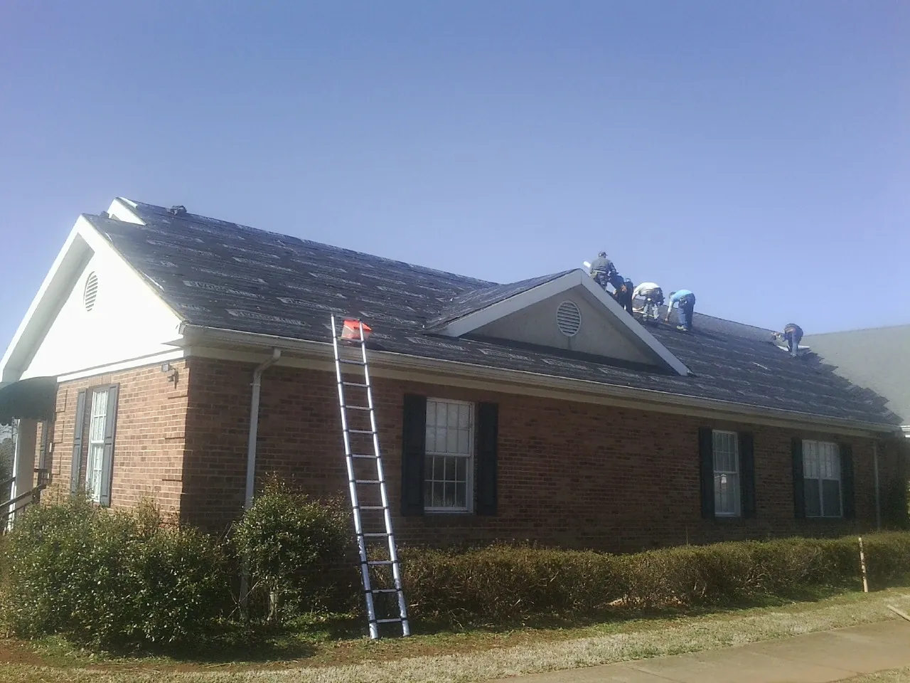Crew tearing shingles off a brick ranch roof with a ladder set — Emergency Roof Repair work by our crew in Hardwick