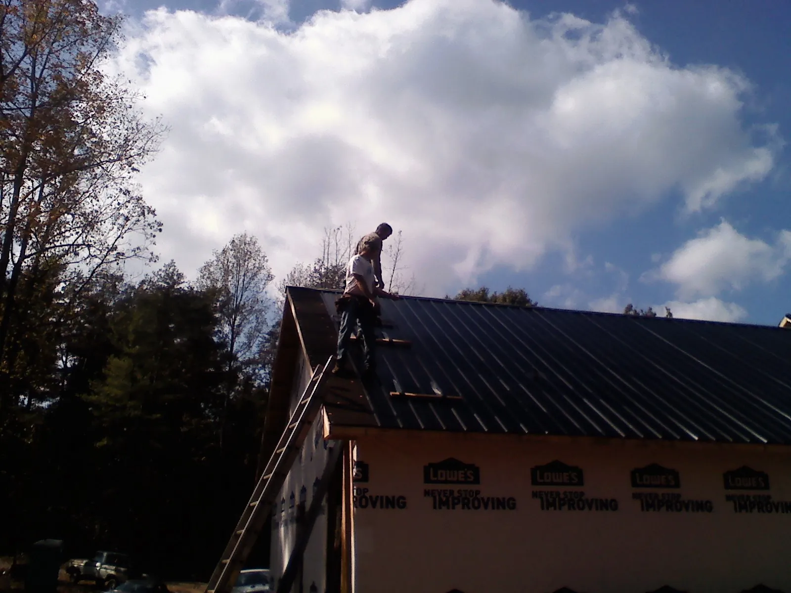 Roofer fastening dark metal panels high against a cloudy sky, from a Roof Inspection job in Hardwick